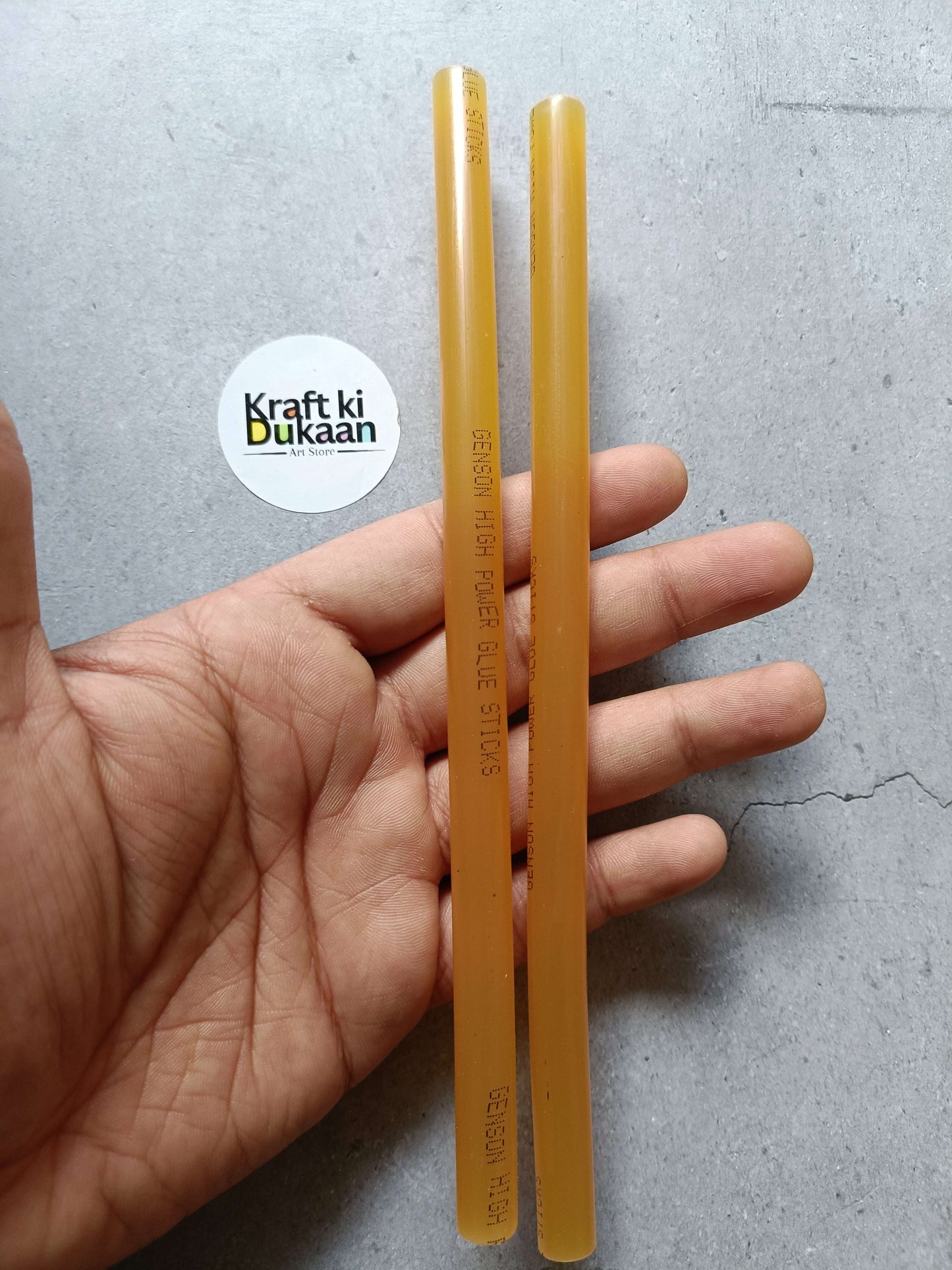 Two amber hot melt glue sticks held in hand, Kraft ki Dukaan label visible