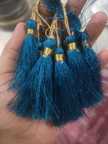 Silk tassels with teal fringe and gold caps, held in an open hand