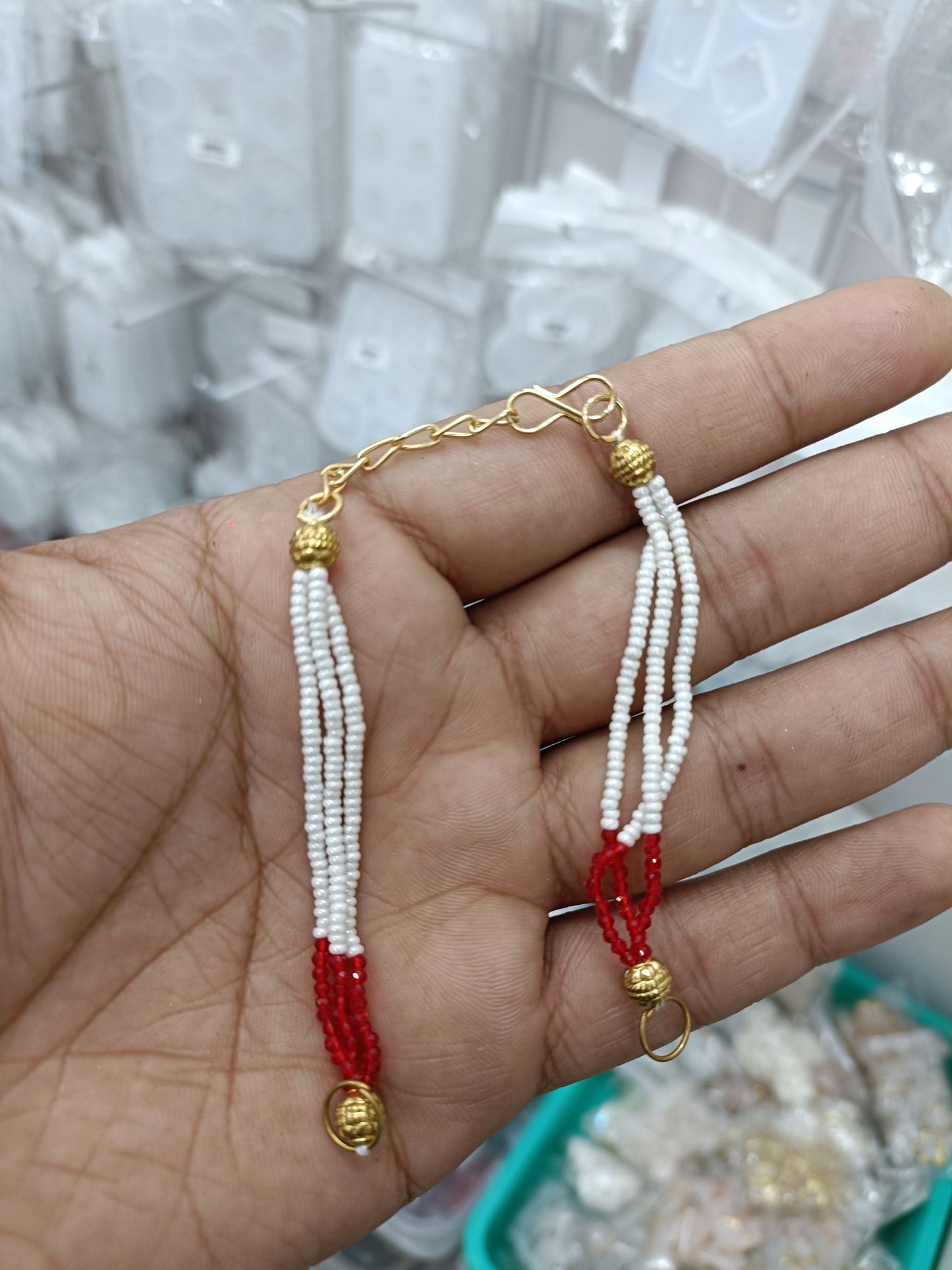 Rakhi bracelet chain with white bead strands, red charm, and gold link clasp