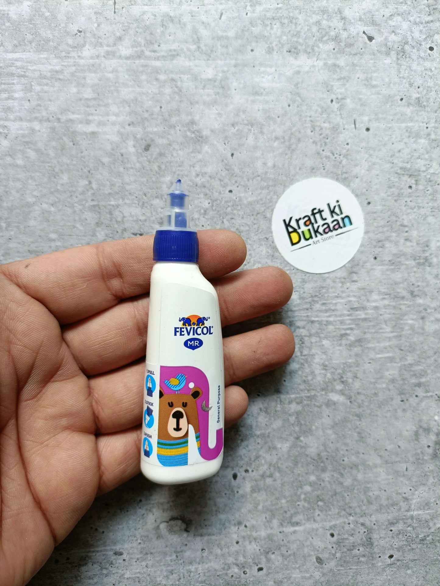 Fevicol MR white glue bottle held in hand, blue cap and bear artwork
