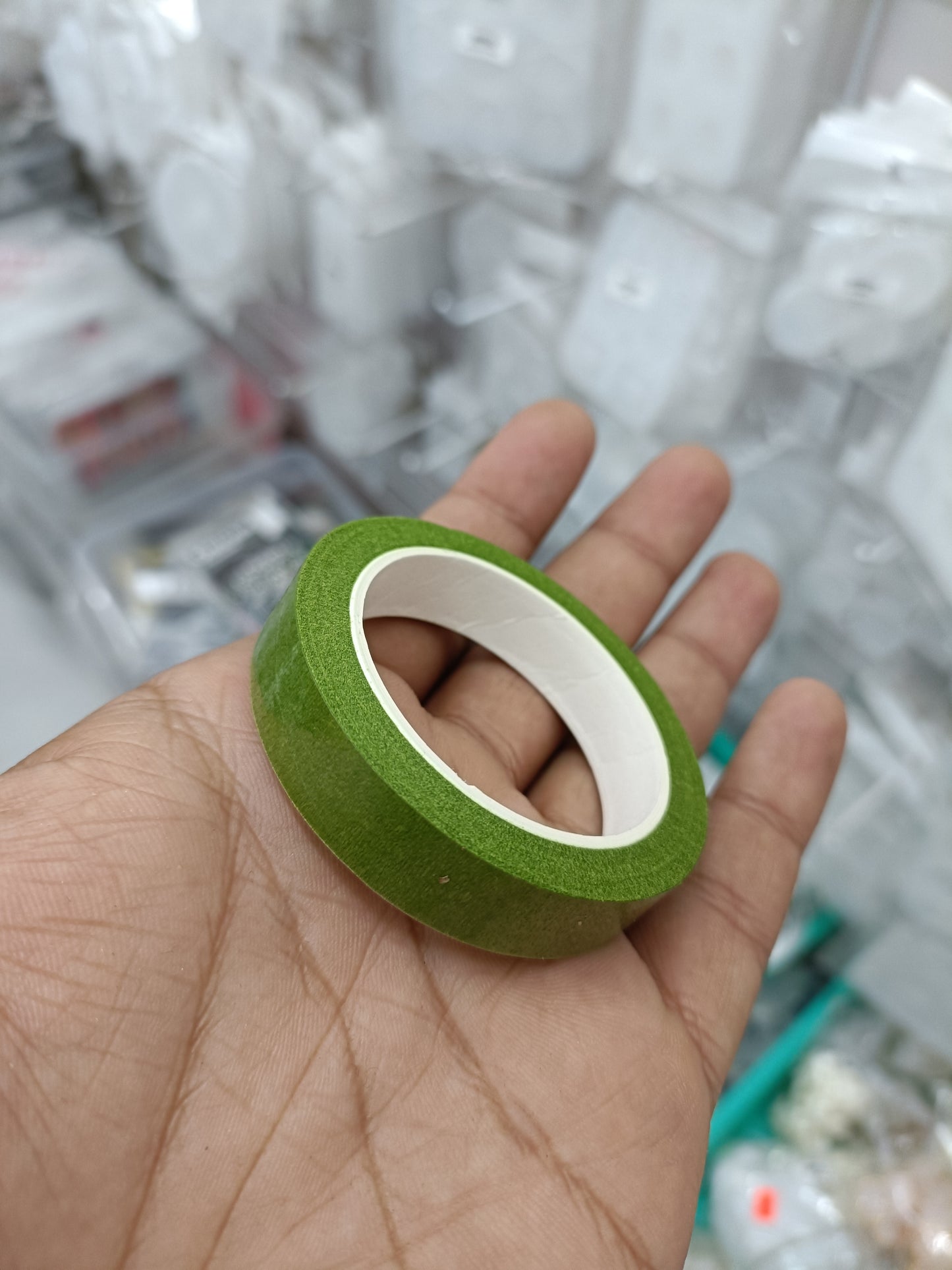 Green floral tape roll with cream adhesive backing, held in hand