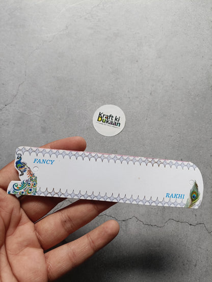 Rakhi greeting card held in hand, white with decorative border and peacock corner art