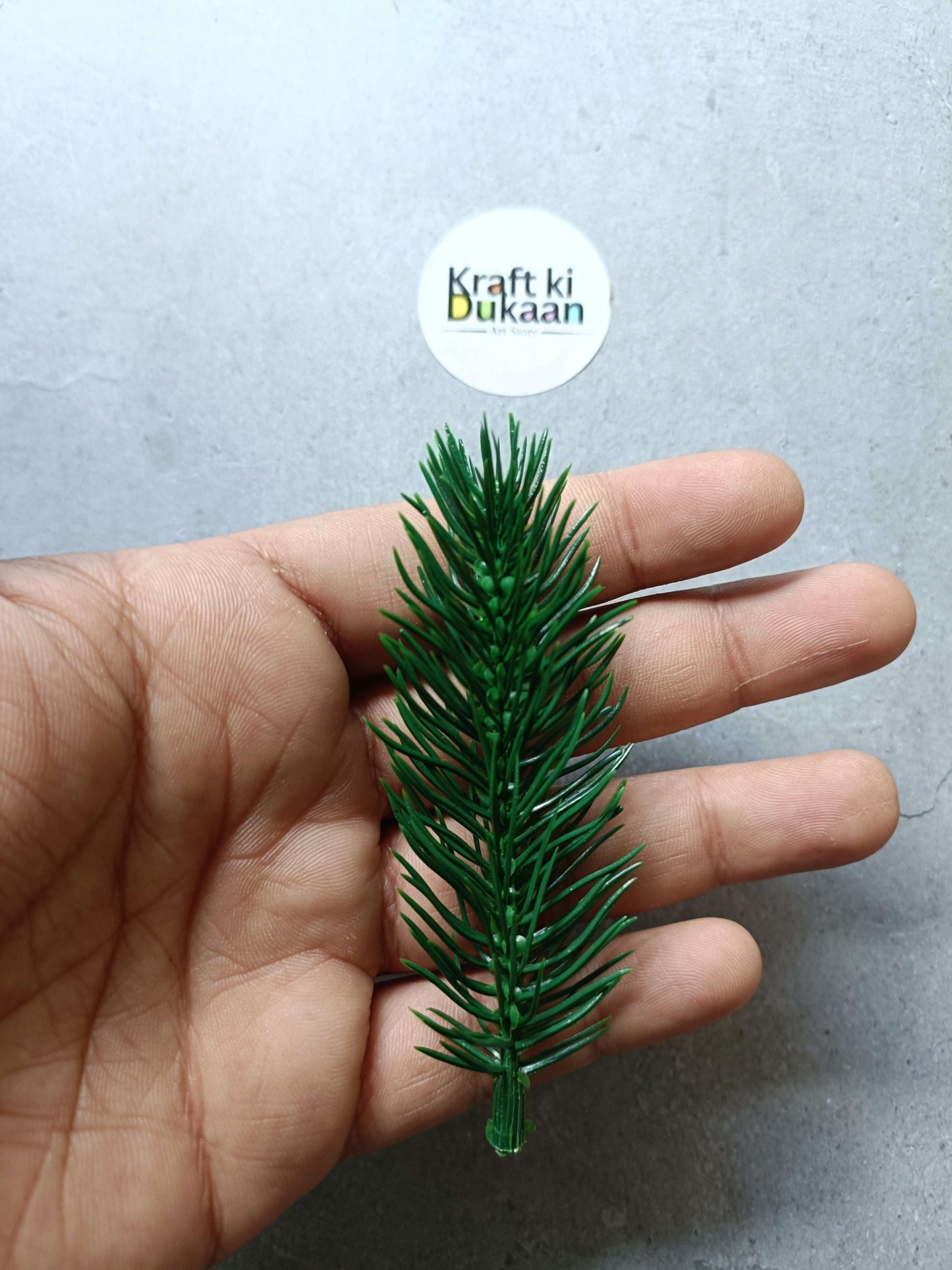 Artificial flower sprig in hand, green pine-like leaves and stem