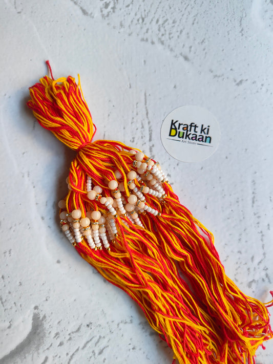 Rakhi dori with red-orange thread and white bead detailing, with hanging charm beads