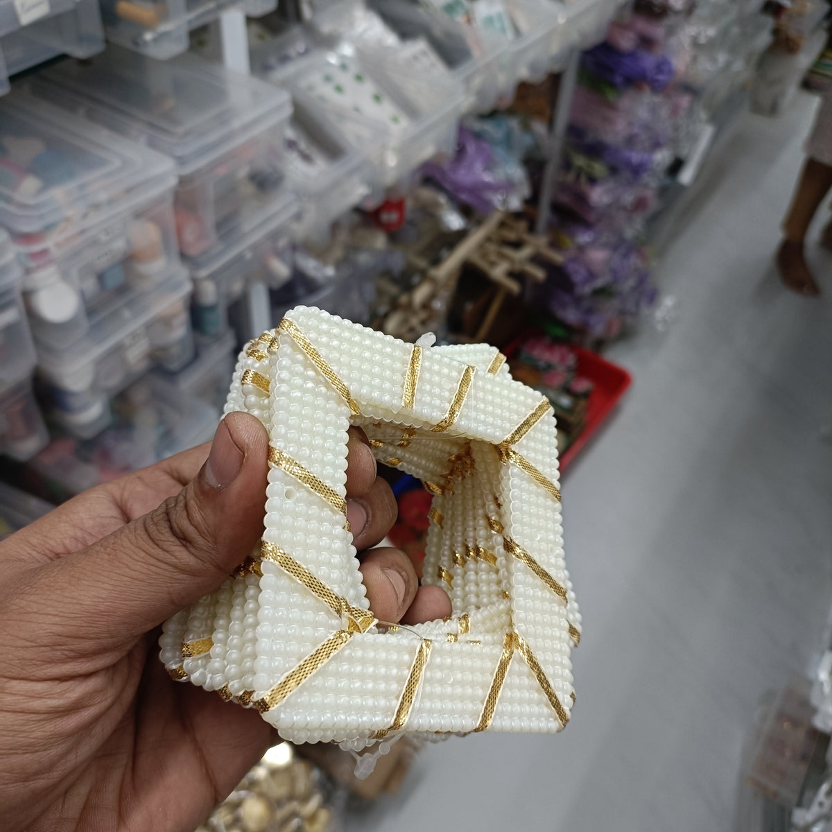 Square beaded ring with white beads and gold trim, held in hand