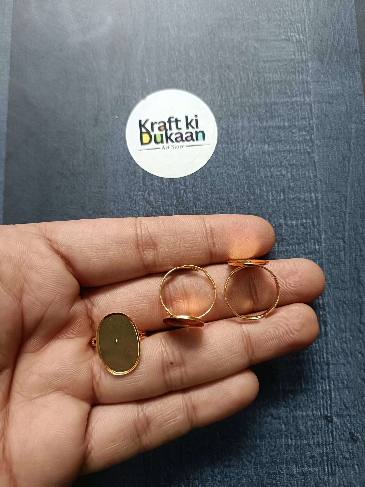 Gold-tone ring bases held in hand: dark round and oval bezel open bands