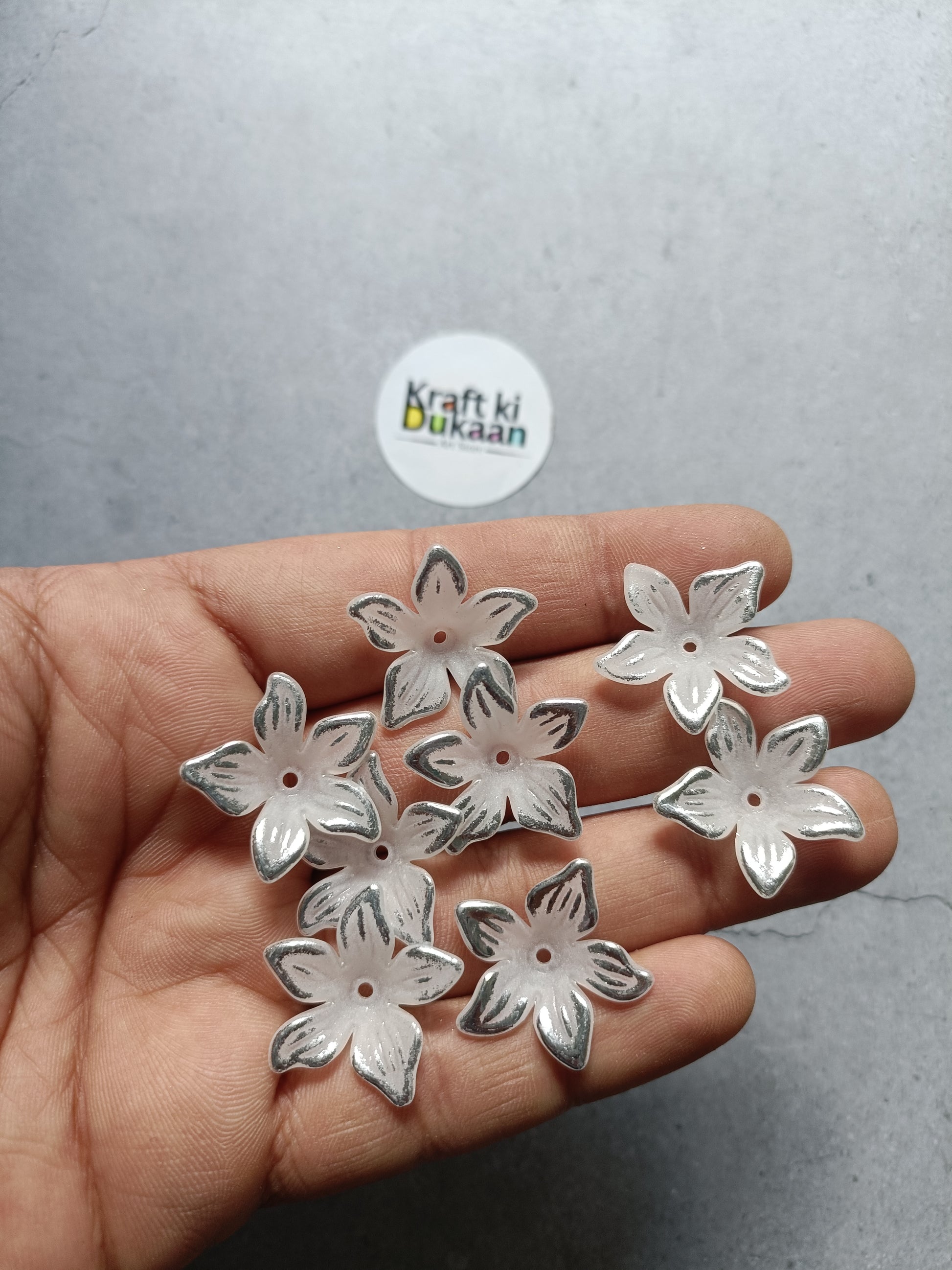 Silver flower-shaped beads, small flat backs, held in hand