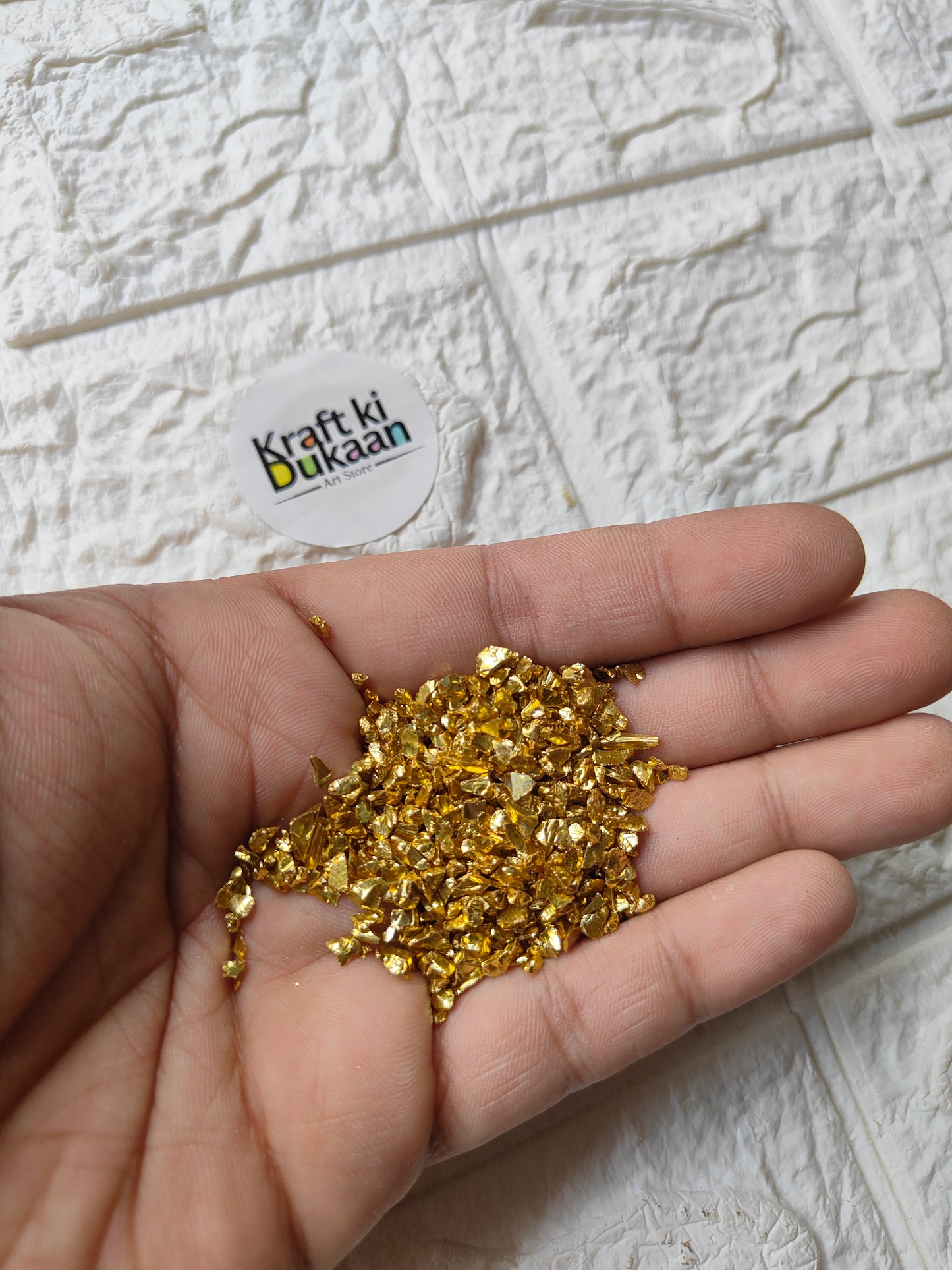 Gold stone granules, small glitter pieces for crafts, shown in palm