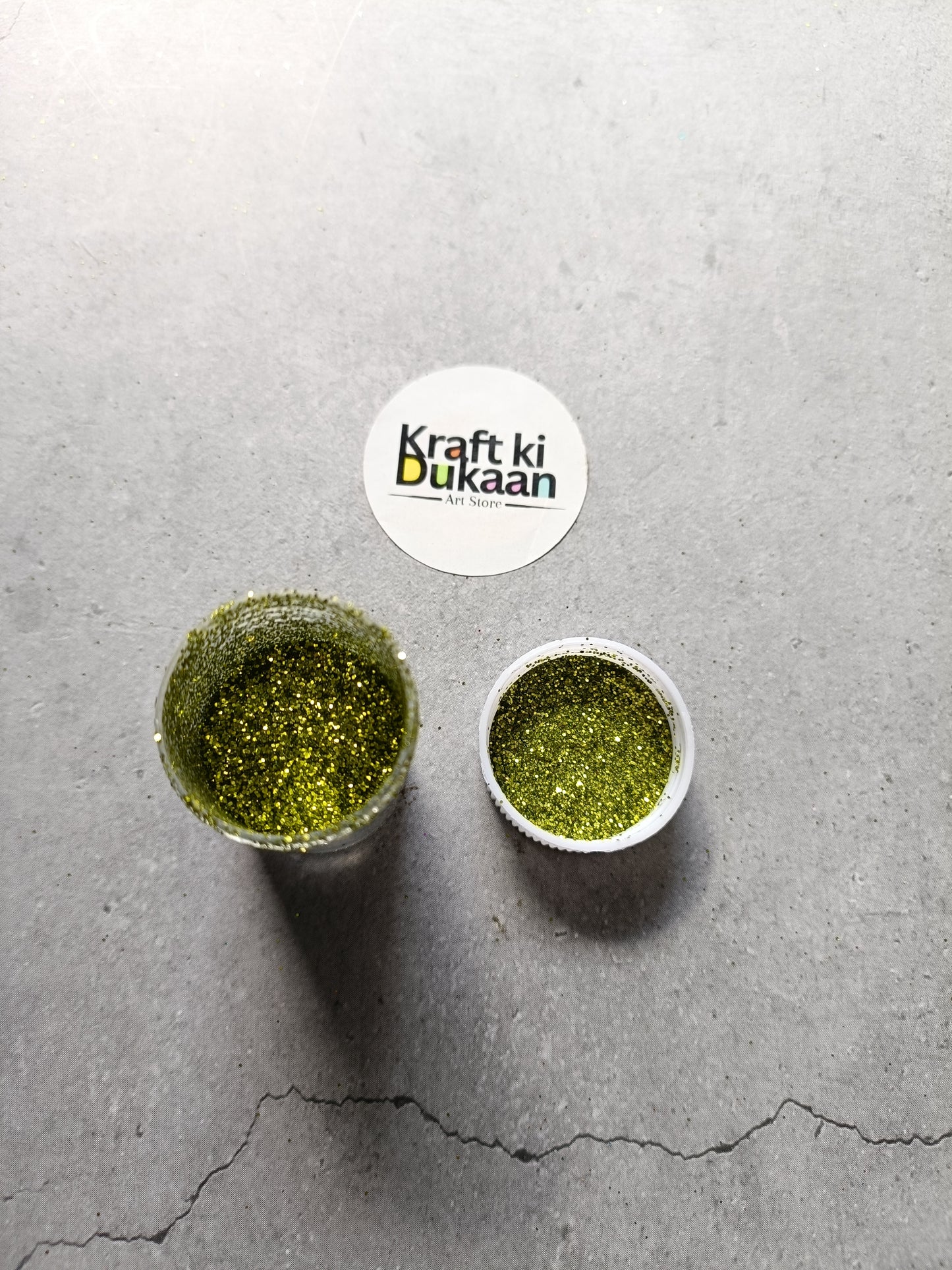 Olive green chunky glitter powder jar with small open cup.