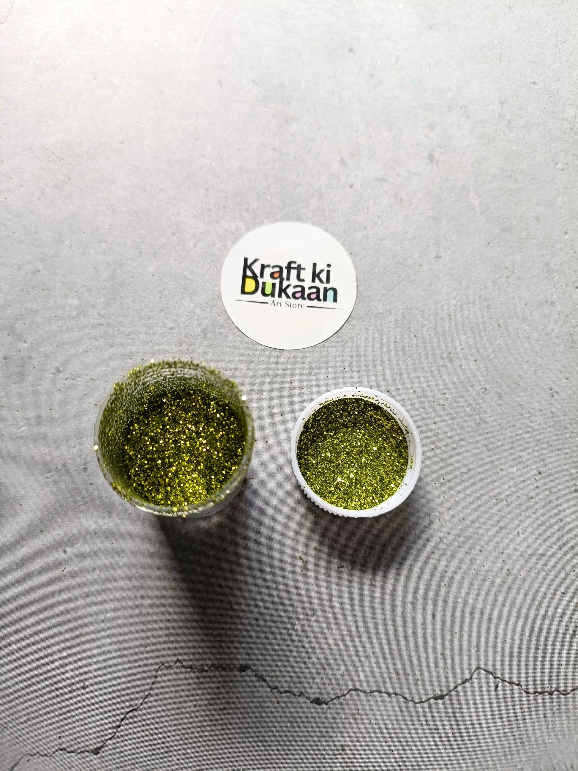 Olive green chunky glitter powder jar with small open cup.