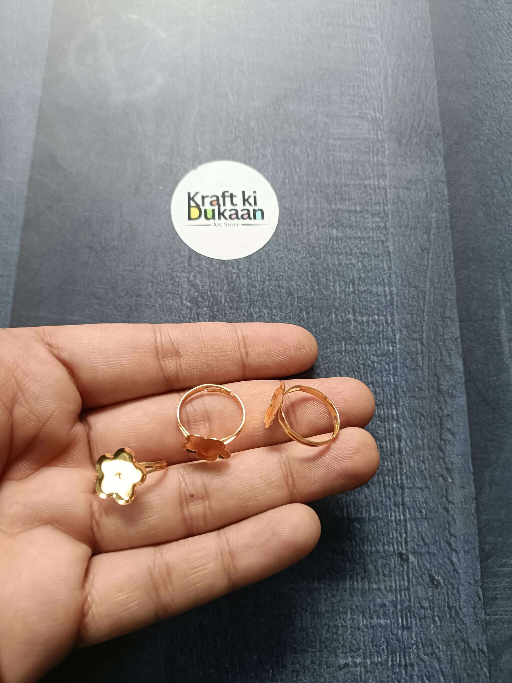 Gold-tone ring bases in hand: clover/flower and round bezel open bands