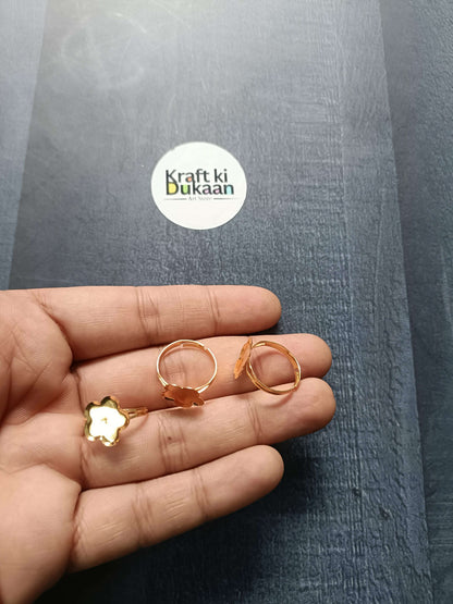 Gold-tone ring bases in hand: clover/flower and round bezel open bands