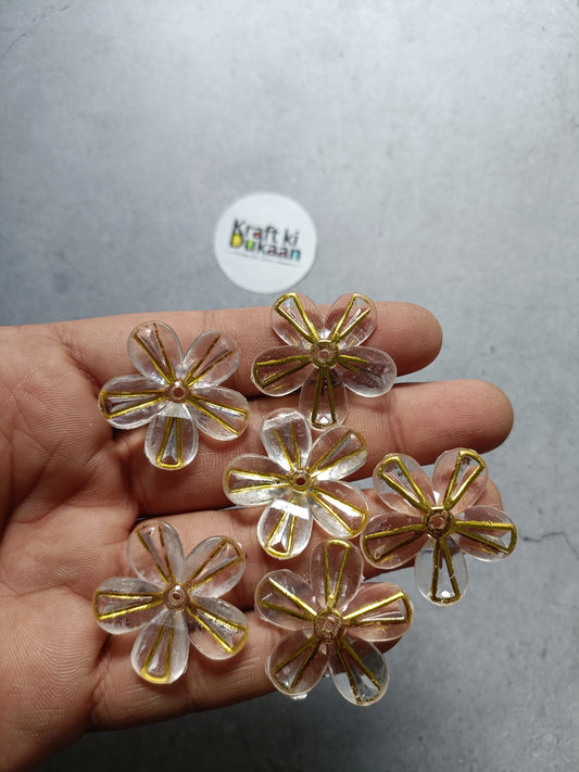 Golden flower bead charms with metallic gold and clear accents, held in hand