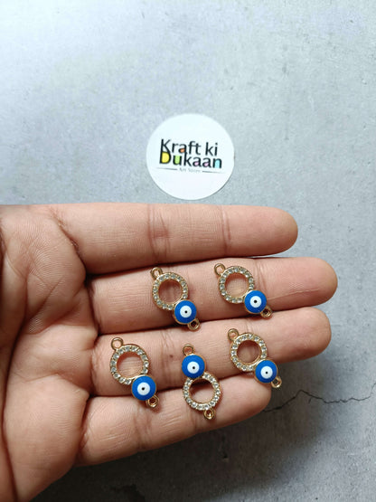 Five evil eye bracelet charms with gold-tone rings and blue eye beads, held in hand