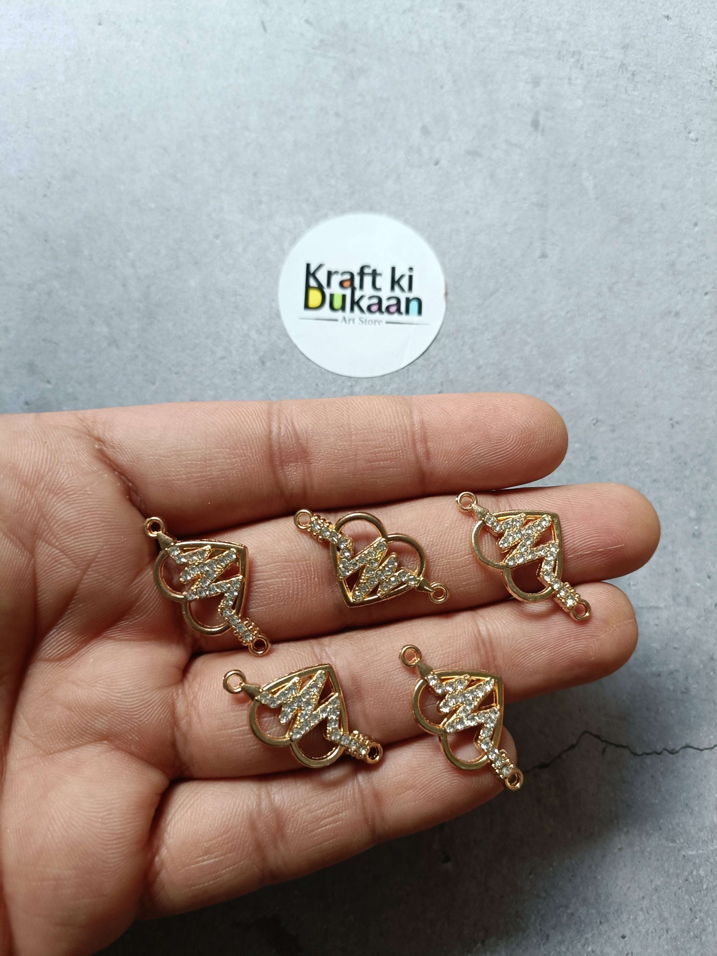 Gold-tone heart-shaped bracelet charms with rhinestone sparkle, held in hand