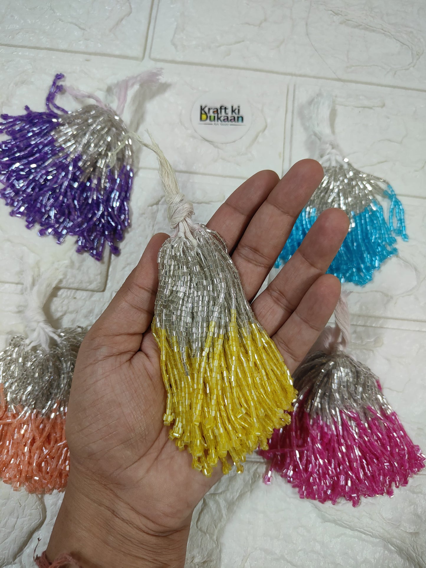 Set of 10 metallic latkan tassels, held in hand: yellow, silver, purple, blue, pink