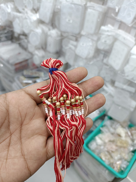 Red and white rakhi dori thread with bead accents, decorative tassels