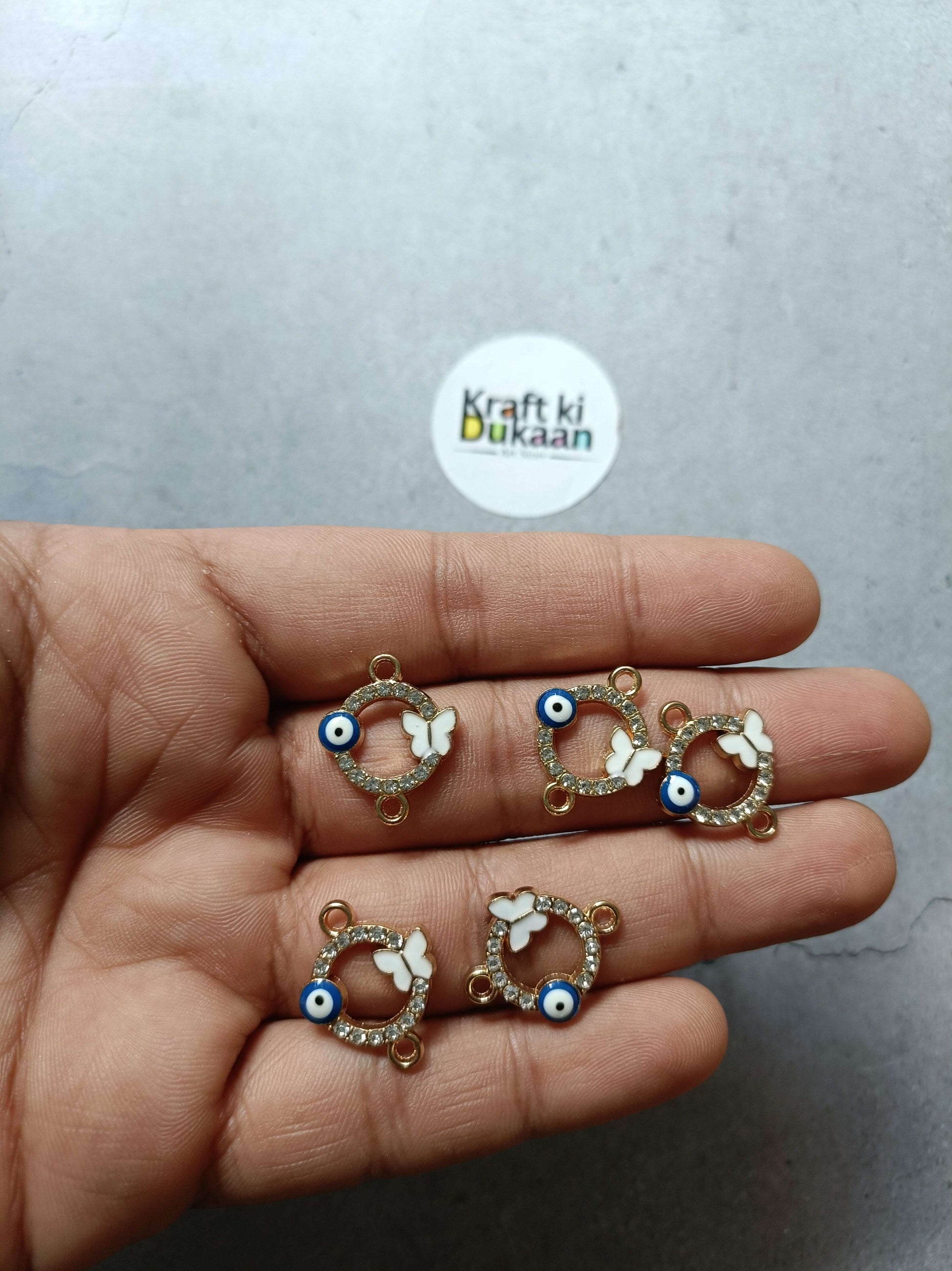 Gold-tone evil eye bracelet charms in hand, white butterfly motifs and blue eyes