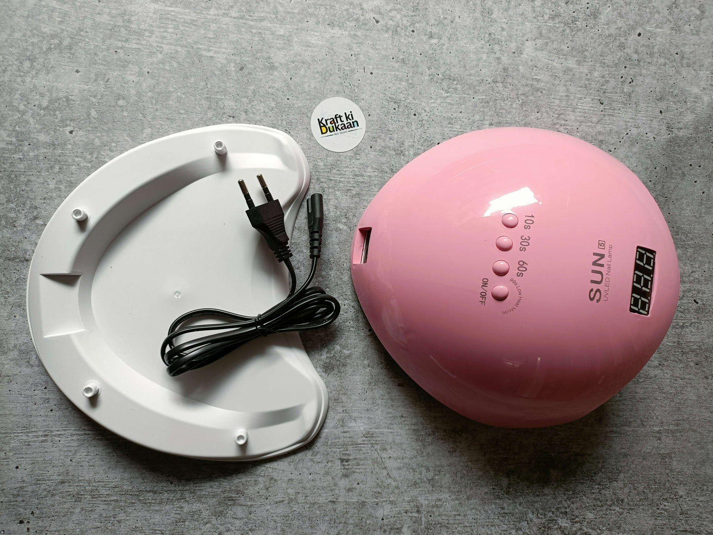 Pink UV LED nail lamp with power cable next to white curing base platform