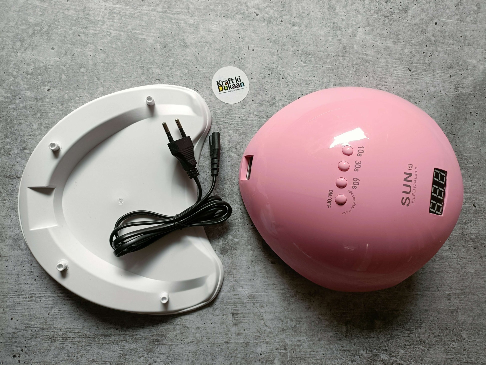 Pink UV LED nail lamp with power cable next to white curing base platform