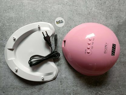 Pink UV LED nail lamp with power cable next to white curing base platform