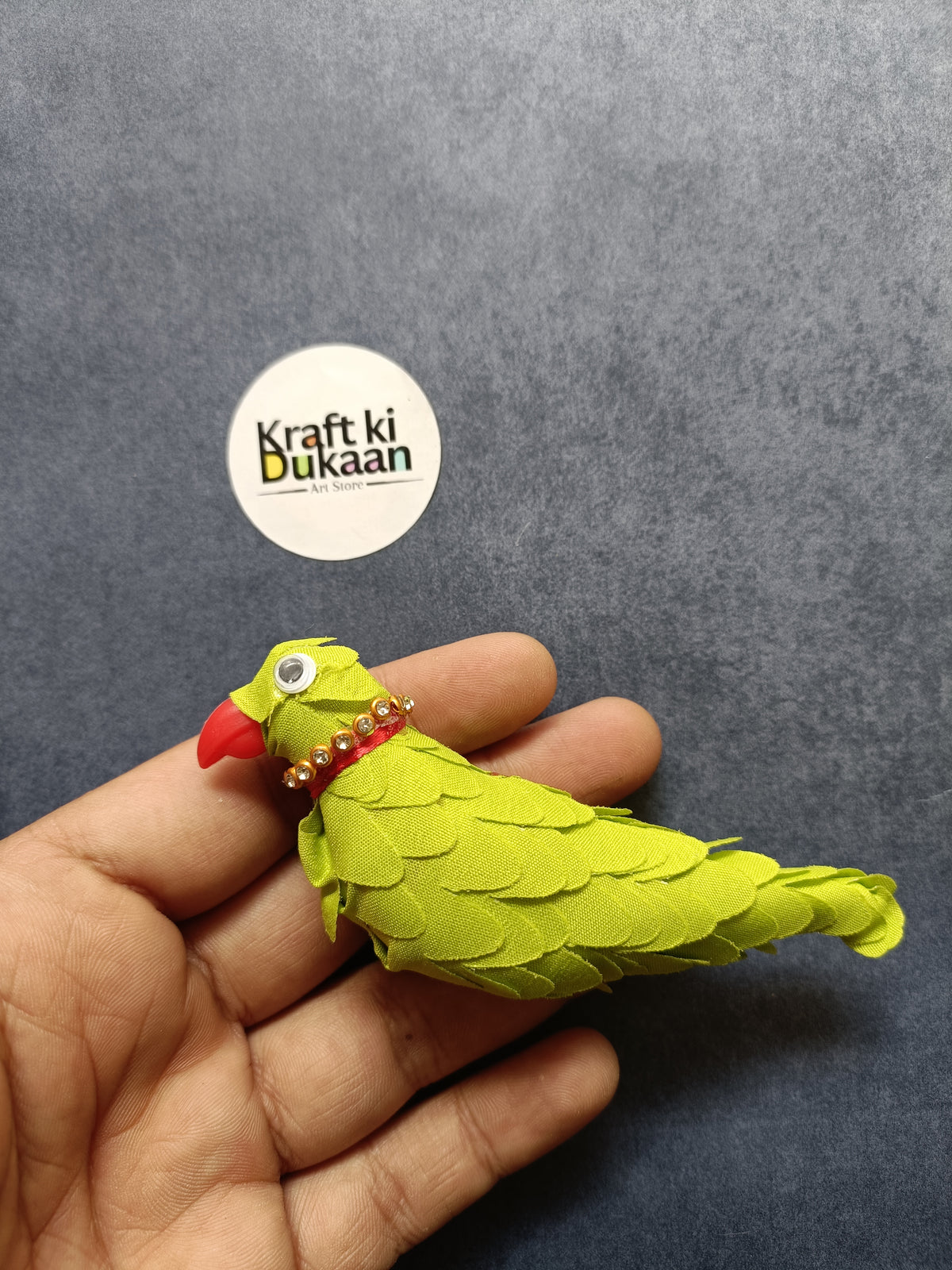 Green parrot figurine held in hand, red beak and jeweled collar