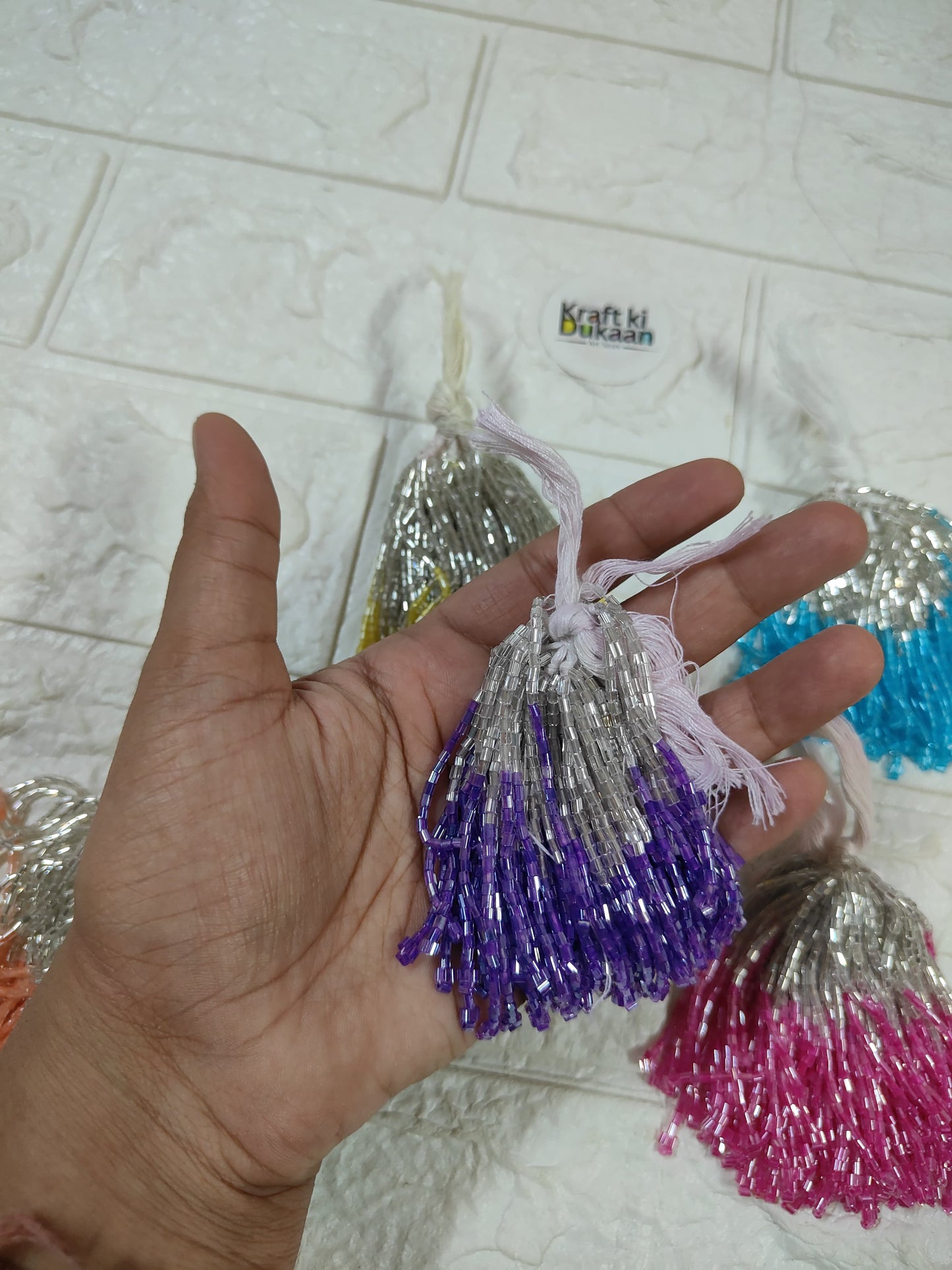 Set of 10 metallic latkan tassels held in hand: silver, purple, and blue tassels