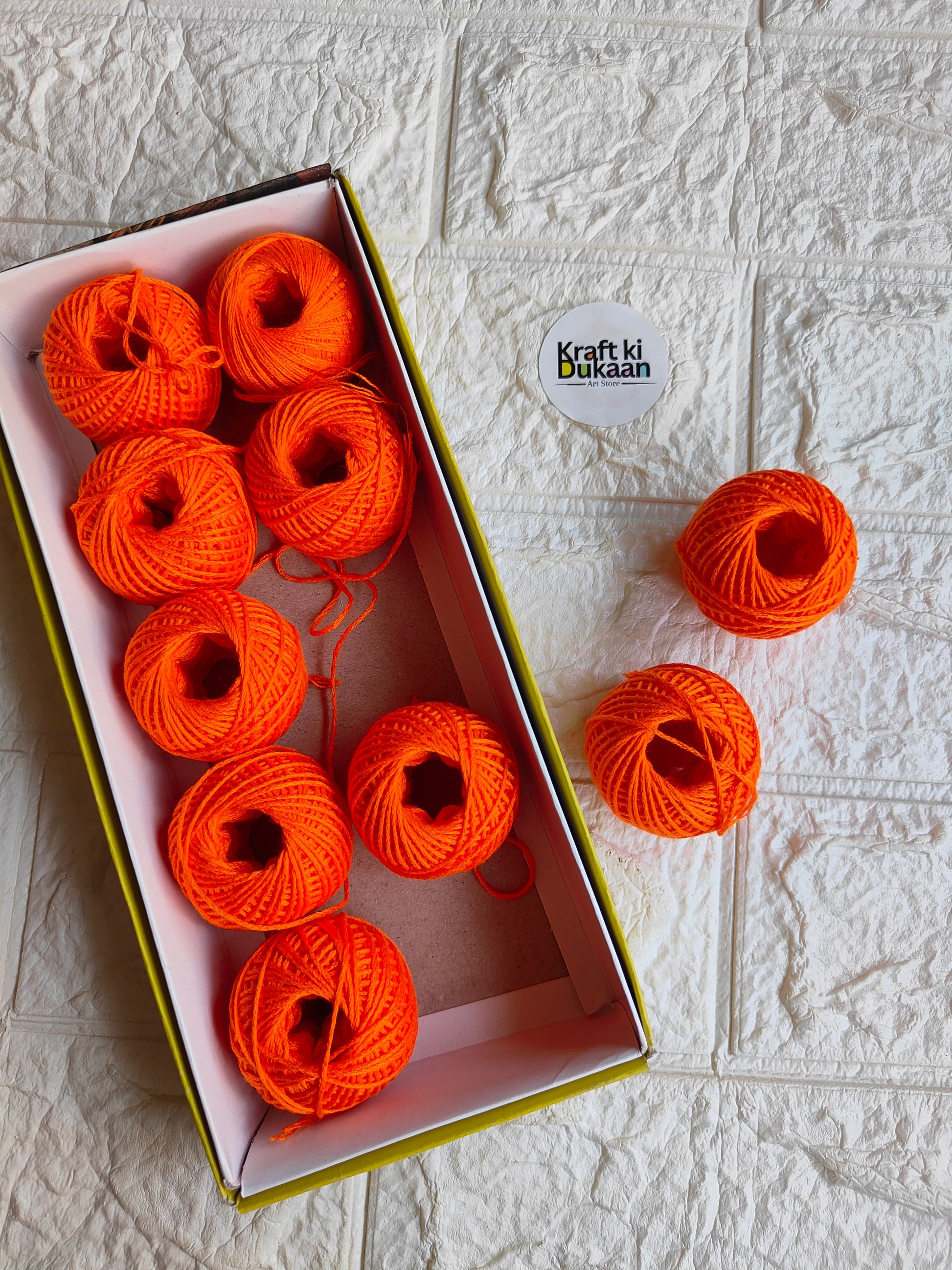 Rakhi thread roll with orange thread balls in open box and one loose ball