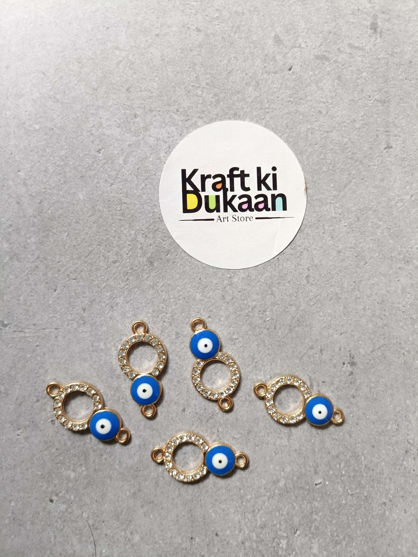 Five evil eye bracelet charms with gold-tone ring settings and blue eye beads, laid out