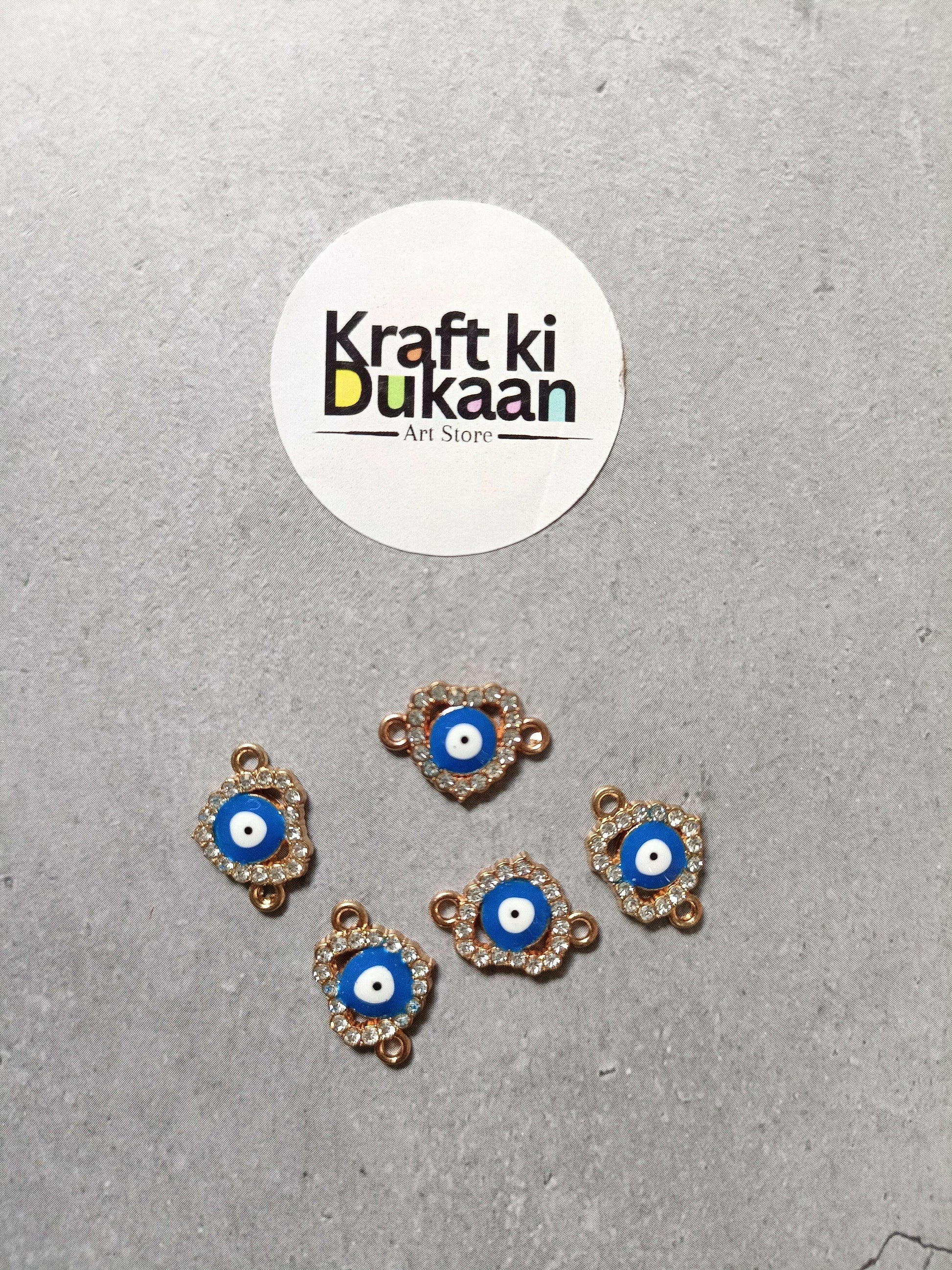 Five evil eye bracelet charms, blue center with gold-tone edging, arranged on surface