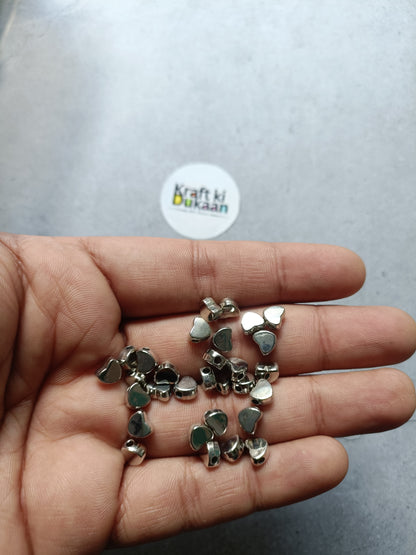 Silver heart-shaped small beads in hand, small metallic pieces for crafts.
