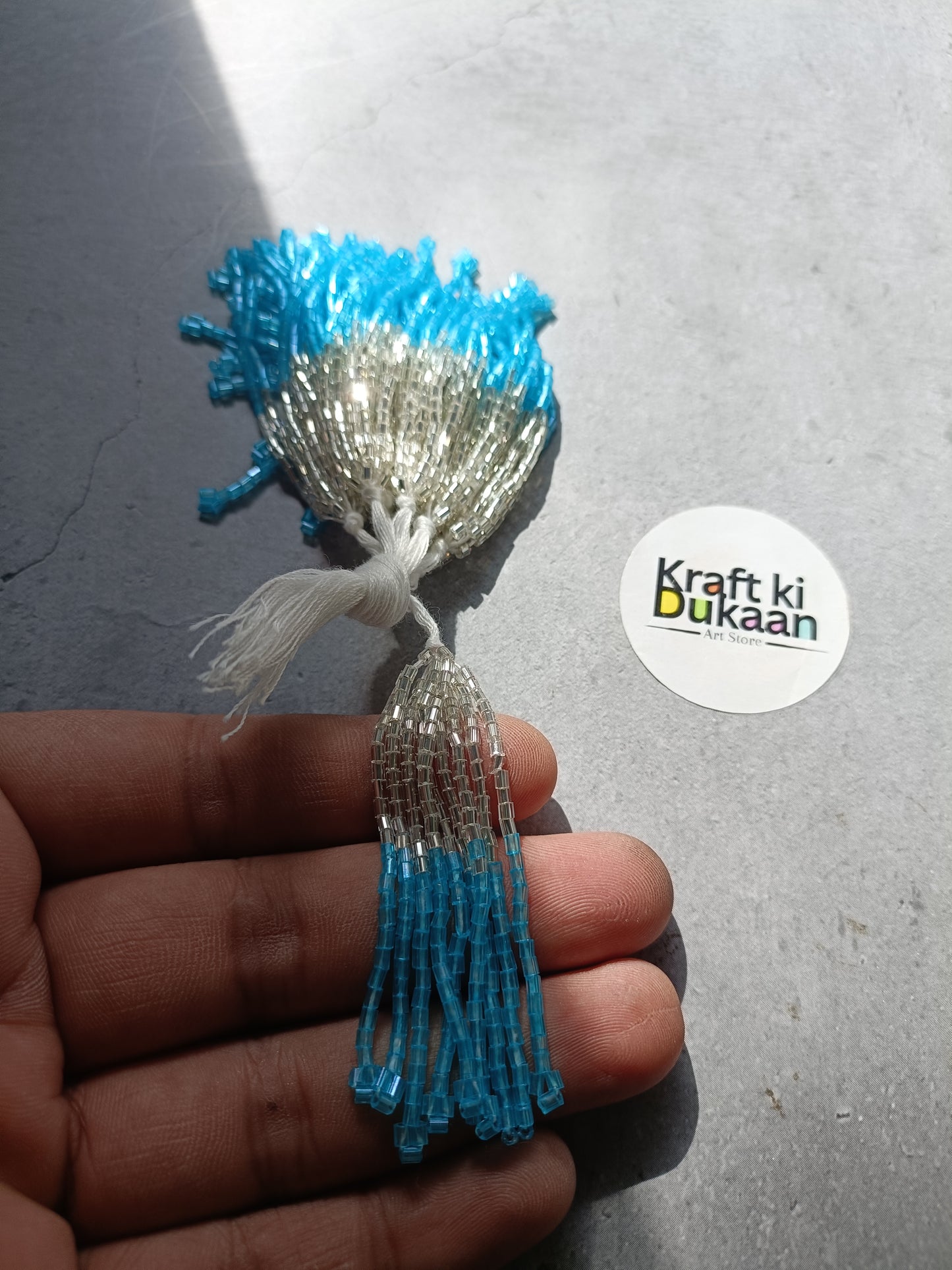 Small beaded tassel latkan with silver top and light blue fringe.