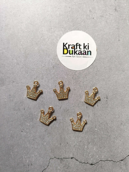 Gold crown pendant charms with rhinestone sparkle, five-piece set laid on surface