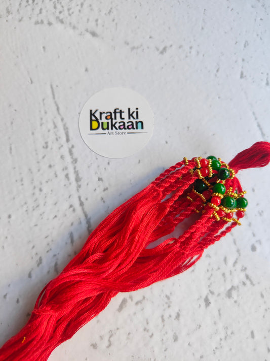 Red rakhi dori with green and gold bead accents and multiple dangling threads