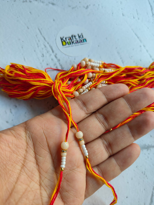 Rakhi dori close-up: red-orange thread, white bead strings, gold accents, on hands