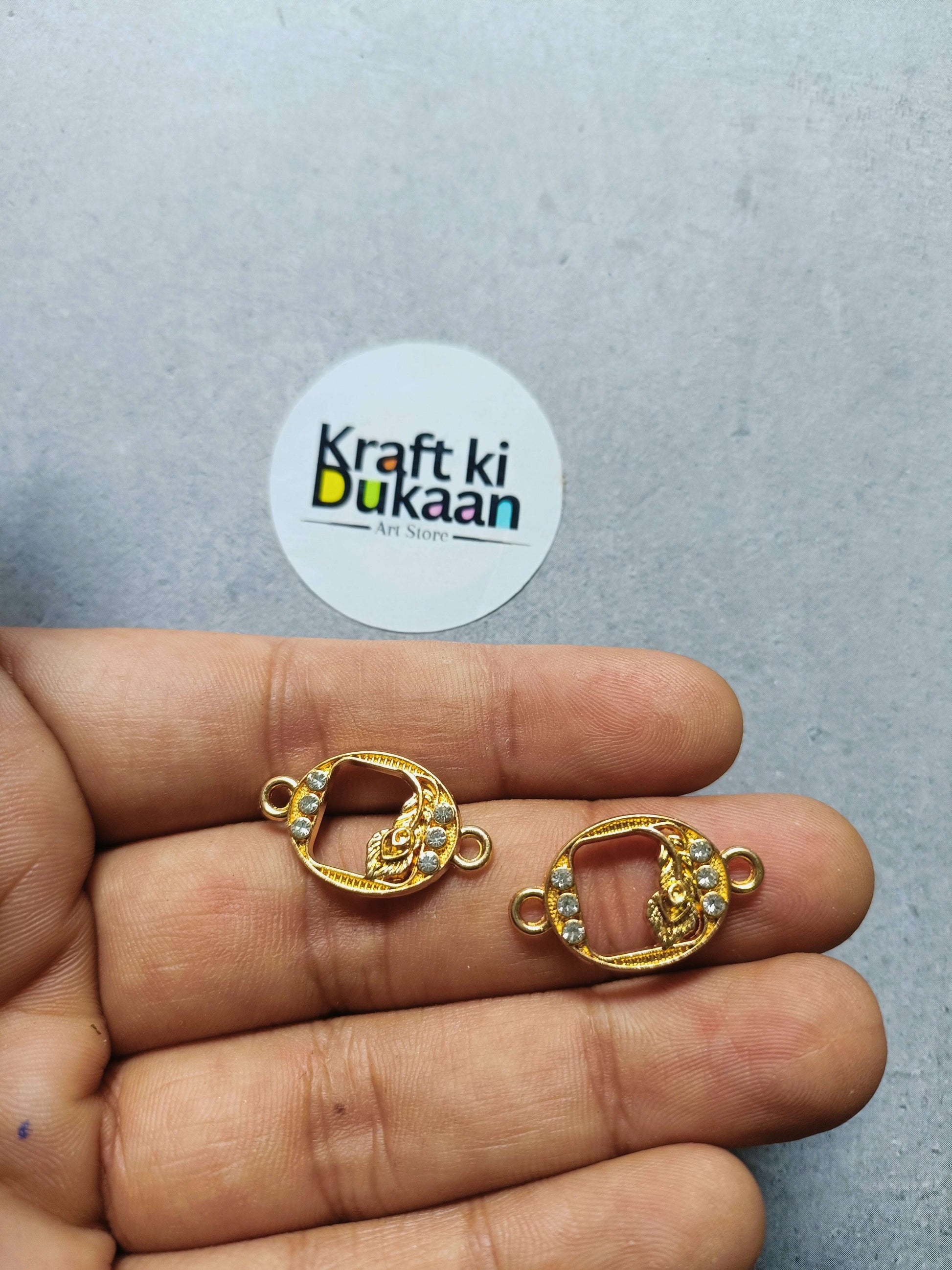 Two gold-tone oval rakhi bracelet bezels with rhinestones held in hand