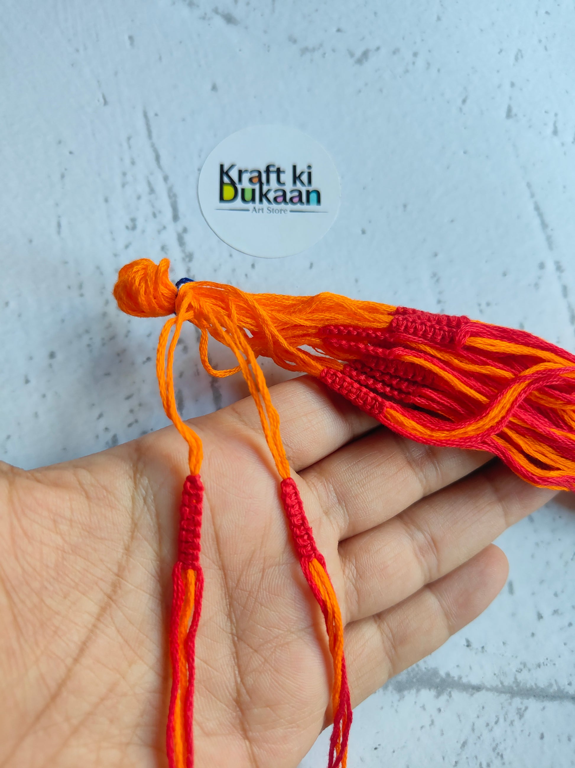 Rakhi dori threads in orange with red accents, held in hand