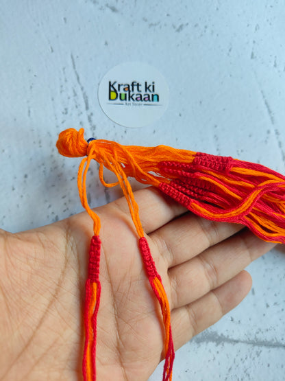 Rakhi dori threads in orange with red accents, held in hand