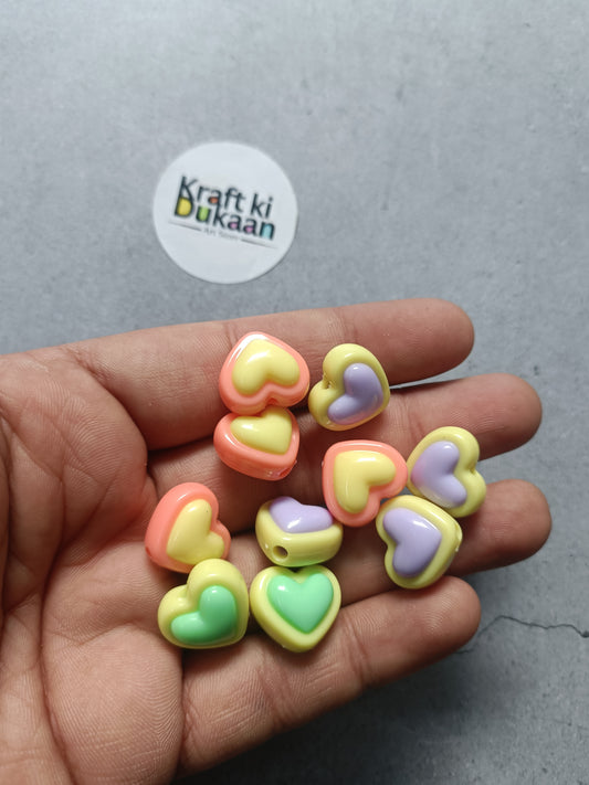 Heart-shaped rakhi bracelet beads in pastel pink, yellow, green, and lavender held in hand