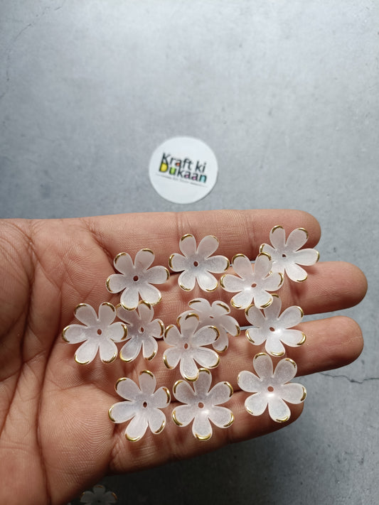 White flower-shaped beads with gold-tone metal loops, held in hand
