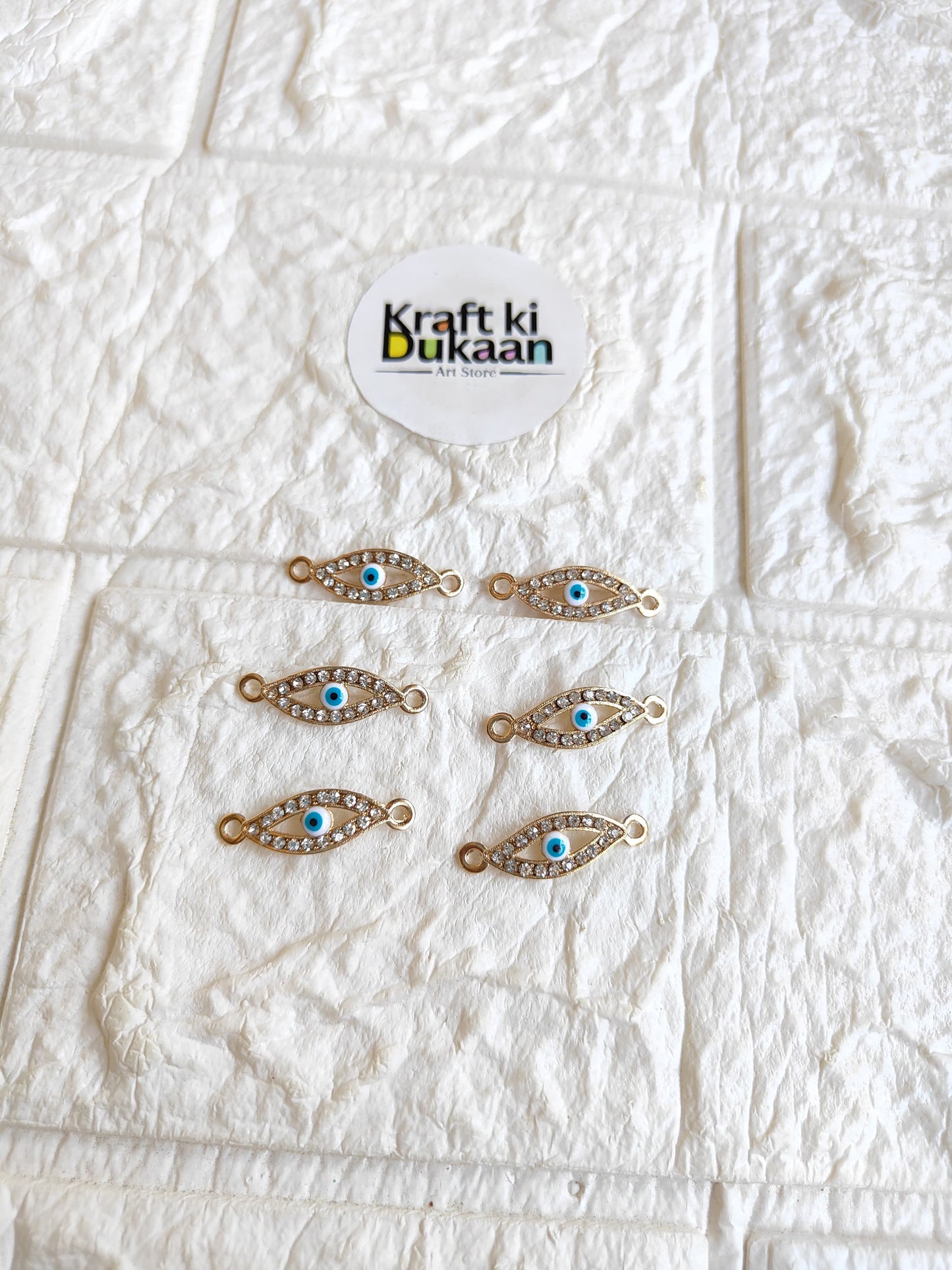 Pack of 5 gold-tone rakhi bracelet pendants with blue oval eye motifs, laid out