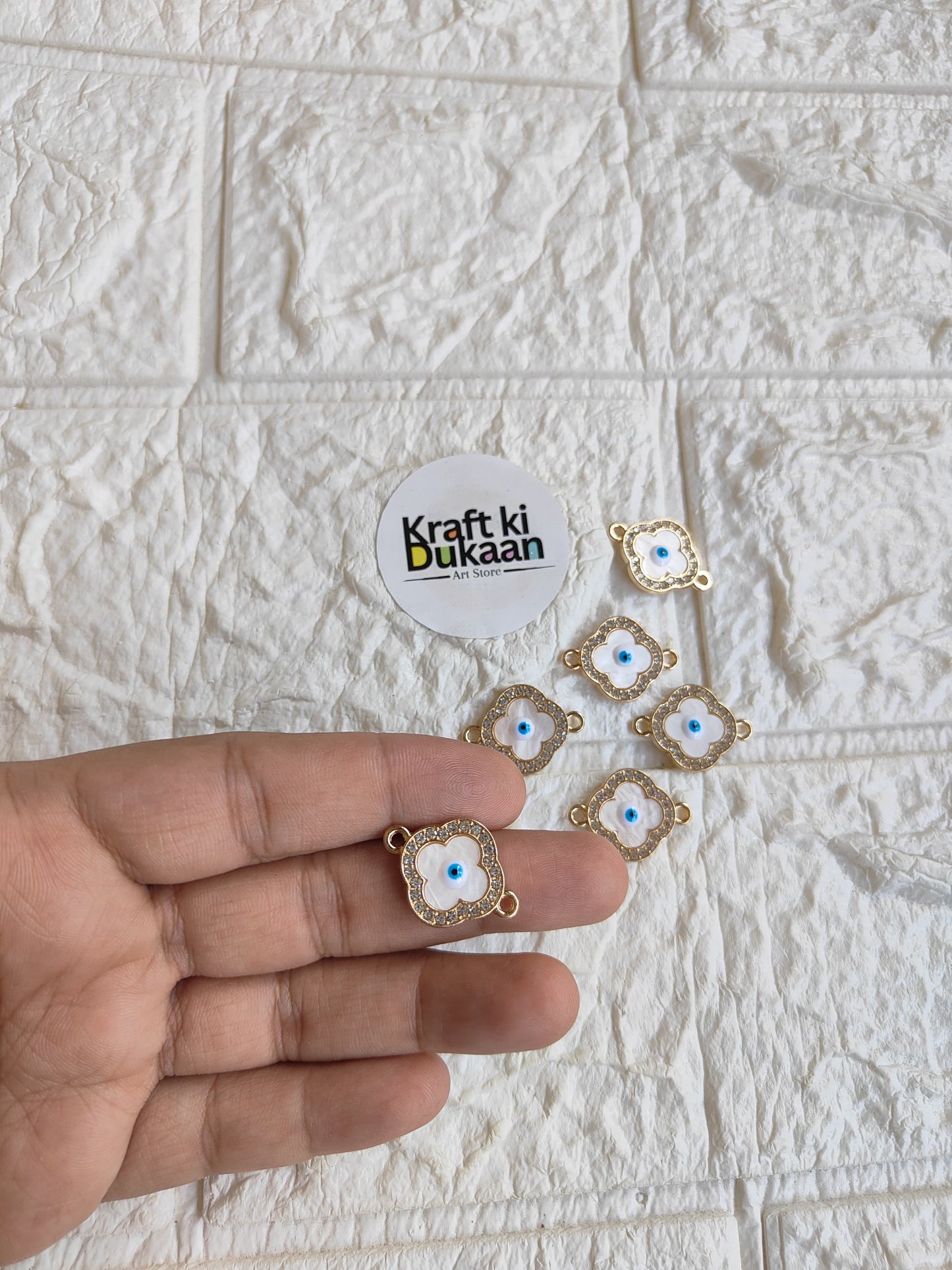 Gold-tone rakhi bracelet pendants with blue evil-eye motifs, held in hand