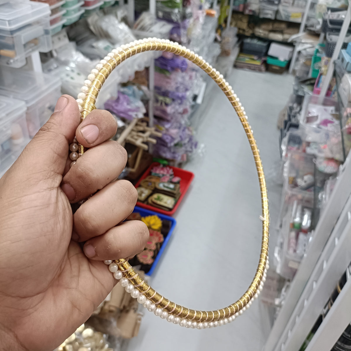 Gold-tone round hoop ring with white pearl beads, held in hand