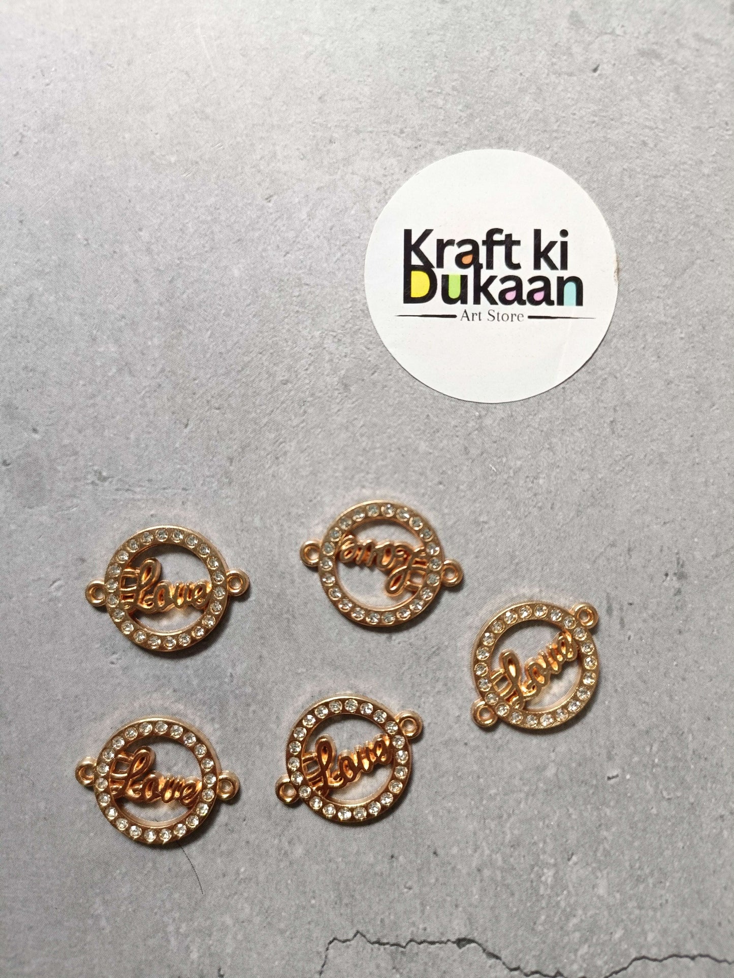 Five gold-tone round Love charms with rhinestone frames and side loops
