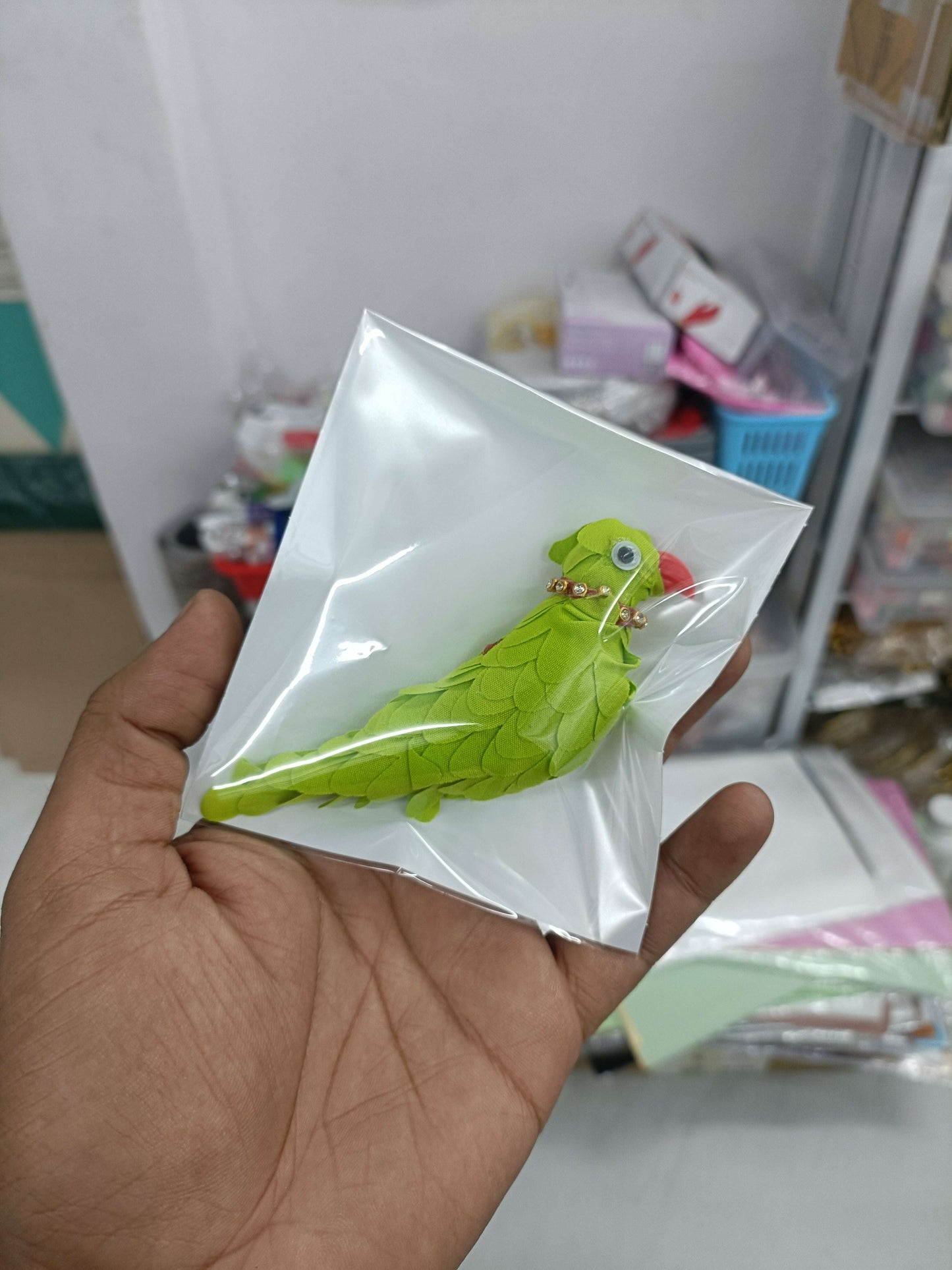 Green parrot-shaped fabric pin with bead eyes, packaged in clear plastic sleeve