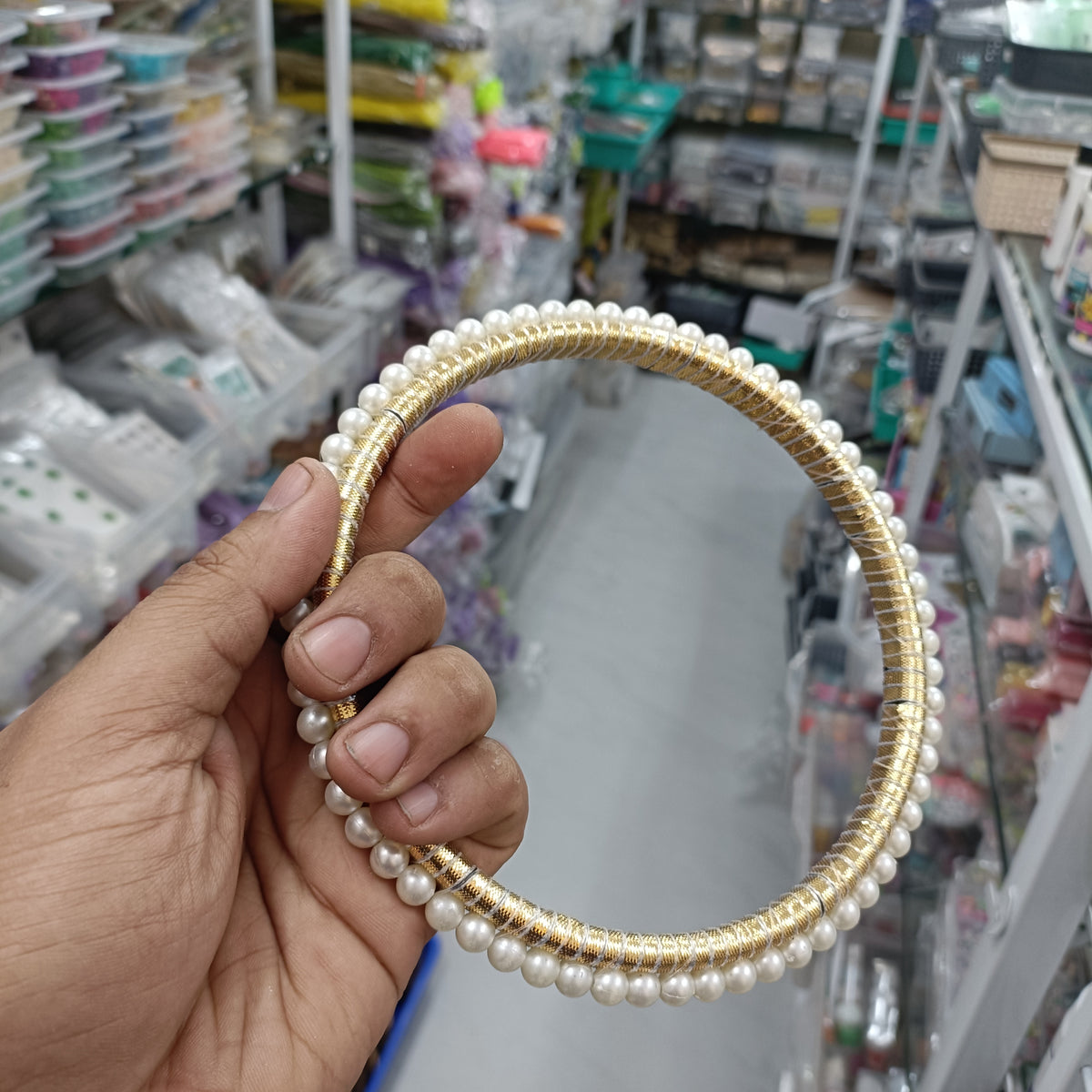 Pearl round ring with white beads and gold-tone beaded edge, held in hand