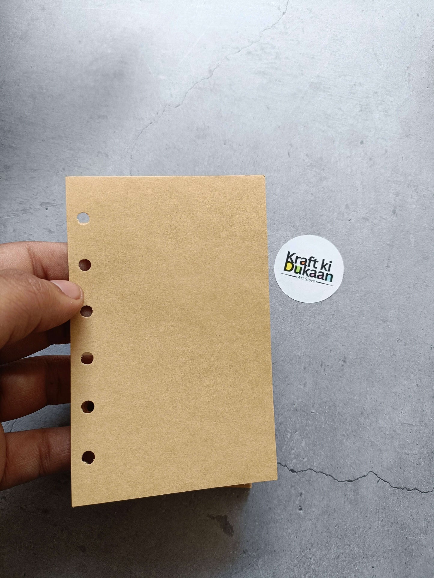 Light brown paper pages with punched hole strip, held in hand