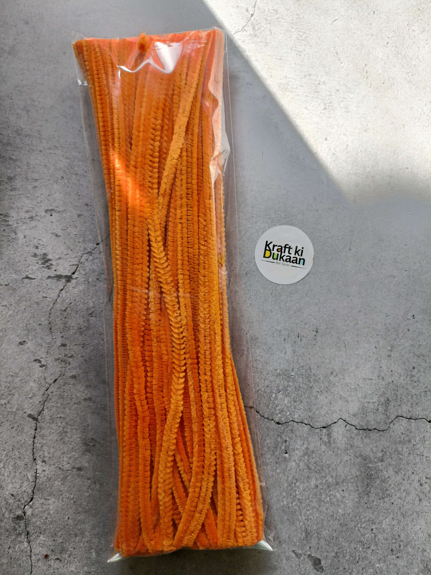 Orange pipe cleaners bundle in clear packaging, fuzzy chenille texture.