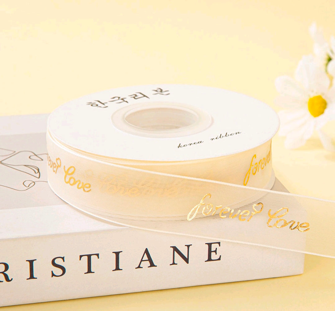 Cream ribbon roll with gold script print, 2.5 cm wide, on spool