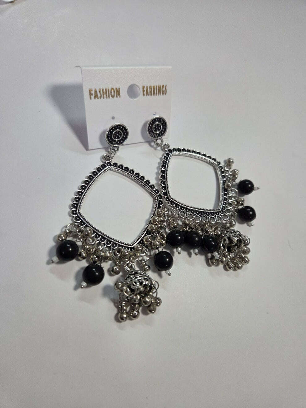 Square jhumka earrings with black beads, silver-tone filigree trim, and bell tassels